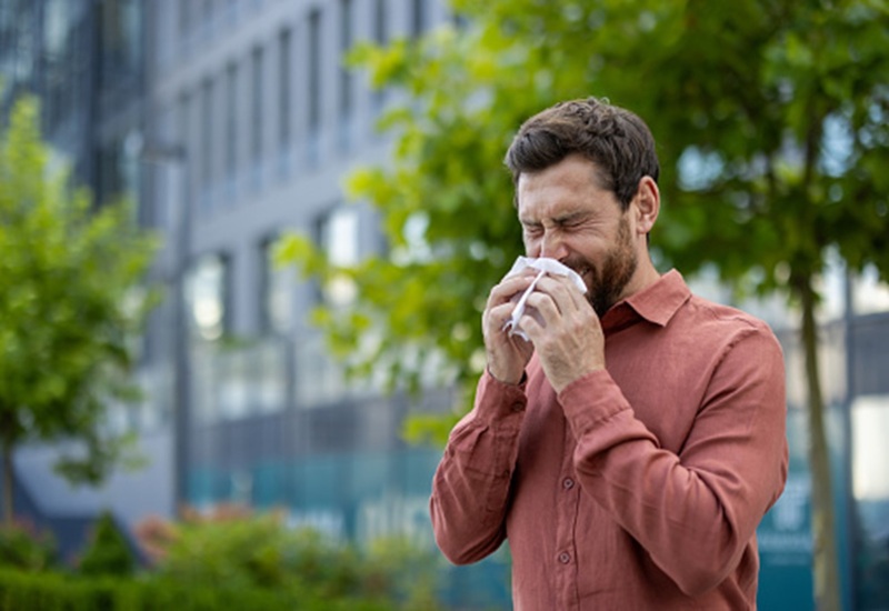 A man stands outdoors, blowing his nose into a tissue IN Knoxville, TN